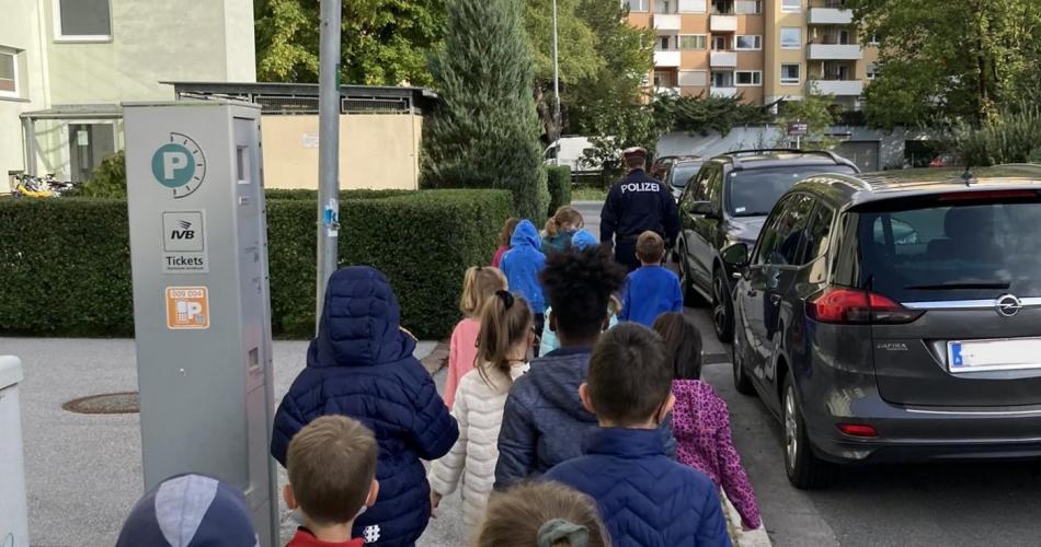 Kinder gehen in Zweierreihe hinter einem Polizisten